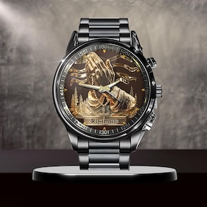 Puede incluir: Un reloj de pulsera negro con un dise&ntilde;o dorado detallado en la esfera, que presenta manos rezando y el nombre "RICHARD". El reloj tiene una correa de metal negro y una esfera redonda con marcadores de tiempo.