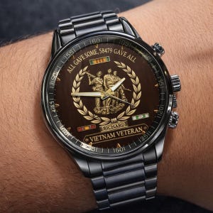 May include: A dark brown watch with a stainless steel band. The watch face features a gold emblem of soldiers, the text "ALL GAVE SOME, 58479 GAVE ALL", and "VIETNAM VETERAN". The watch has a round face and a metal band.