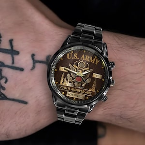 May include: Black wristwatch with a brown face featuring the text "U.S. ARMY" and an eagle emblem. The watch also displays "250TH ANNIVERSARY" and the name "RICHARD". The watch is on a black metal band.