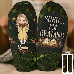 May include: A pair of dark green socks featuring a cartoon character with blonde hair reading a book and holding a glass, with the name Lucia printed below. The other sock displays the text SHHH... I'M READING above an open book illustration.