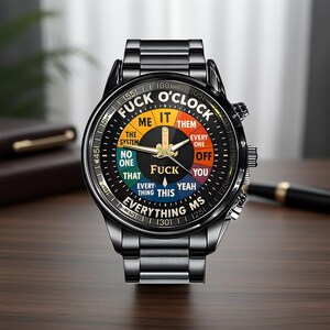 May include: Black wristwatch with a round face featuring the text "FUCK O'CLOCK" in a circular design. The watch face has a black background with colorful segments and gold hands. The watch band is black metal.