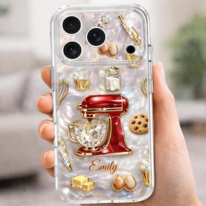 May include: Clear phone case with a pearlized background and gold accents. Features a red stand mixer, cupcakes, eggs, and a chocolate chip cookie. The name "Emily" is written in gold script.