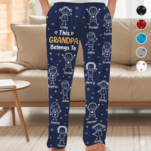 May include: Dark blue pajama trousers featuring white illustrations of children and stars. The text "This GRANDPA Belongs To" is printed in gold, with names below. A comfortable and personalized gift.