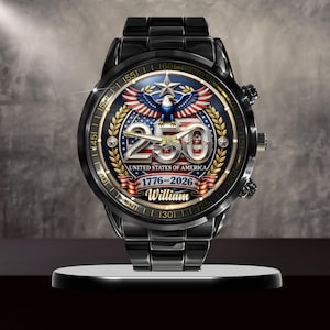 May include: Black wristwatch with a detailed face featuring an eagle, stars, and the text "250 UNITED STATES OF AMERICA 1776-2026 William." The watch has a black metal band and a round face with gold accents.