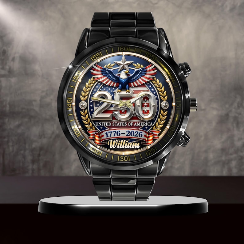 May include: Black wristwatch with a detailed face featuring an eagle, stars, and the text "250 UNITED STATES OF AMERICA 1776-2026 William." The watch has a black metal band and a round face with gold accents.