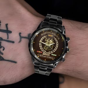 May include: Black wristwatch with a brown face featuring a gold emblem and the text "ALL GAVE SOME, 58479 GAVE ALL". The watch also includes the text "RICHARD" and "VIETNAM VETERAN".