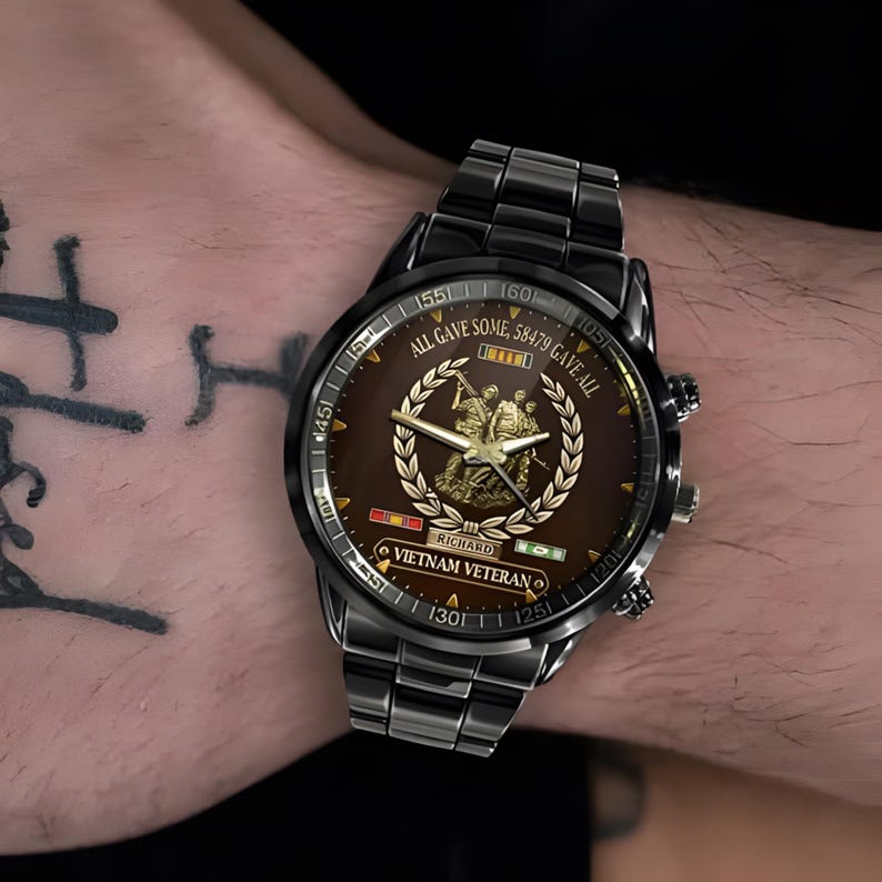 May include: Black wristwatch with a brown face featuring a gold emblem and the text "ALL GAVE SOME, 58479 GAVE ALL". The watch also includes the text "RICHARD" and "VIETNAM VETERAN".