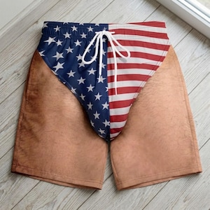 May include: Shorts featuring a print of the American flag on the front panel with a blue field of white stars on the left and red and white stripes on the right. The legs feature a tan skin-tone print with a subtle hair texture pattern. White drawstring.