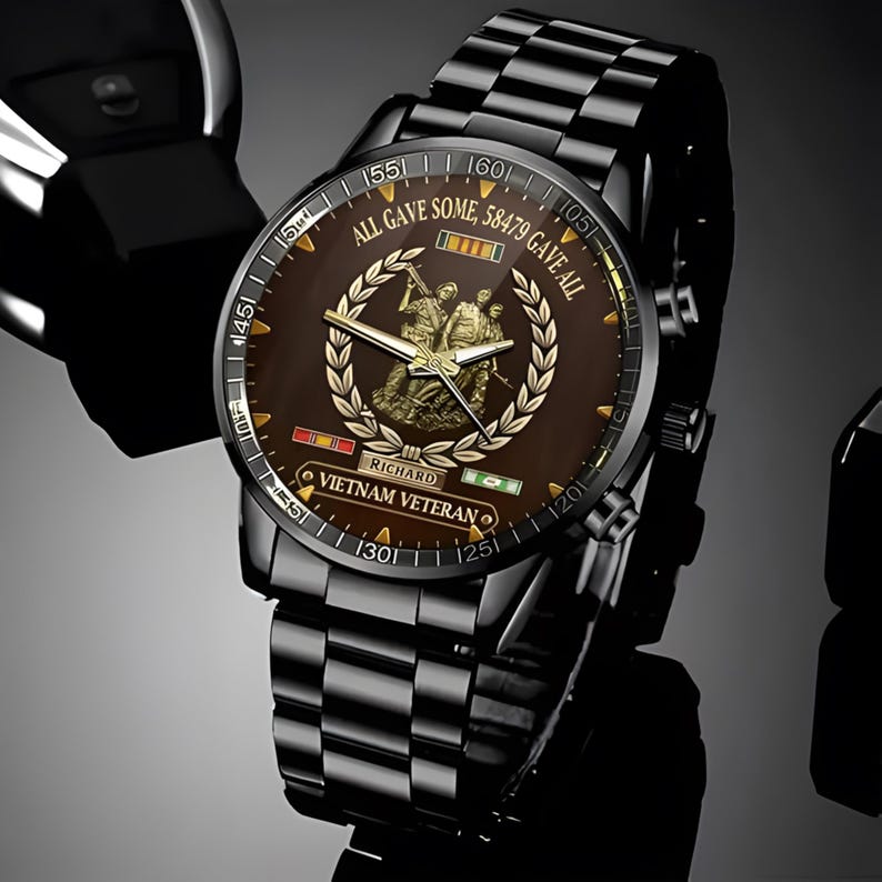 May include: Black wristwatch with a brown face featuring a gold emblem and the text "ALL GAVE SOME, 58479 GAVE ALL". The watch has a black metal band and the words "VIETNAM VETERAN" are visible on the watch face.