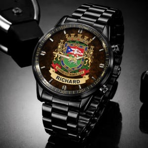May include: Black wristwatch with a brown face featuring a coat of arms design and the name "RICHARD". The watch has a black metal band and a detailed dial with numbers and markings. The watch face includes the text "JOANNES EST NOMEN EJUS".