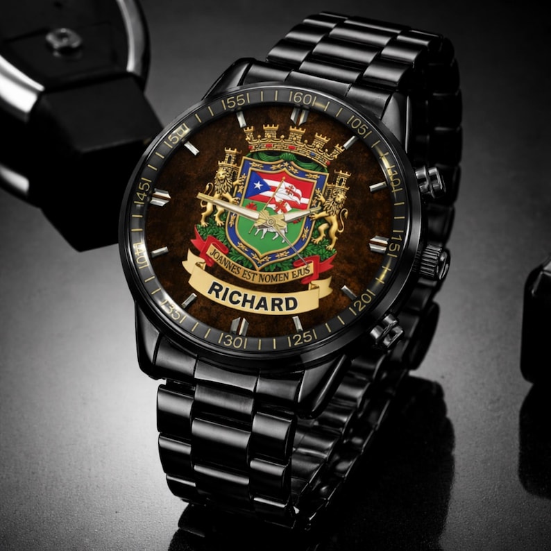May include: Black wristwatch with a brown face featuring a coat of arms design and the name "RICHARD". The watch has a black metal band and a detailed dial with numbers and markings. The watch face includes the text "JOANNES EST NOMEN EJUS".