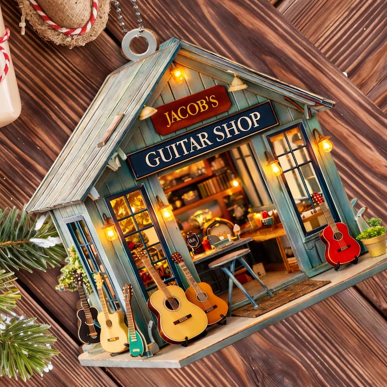 May include: A miniature guitar shop ornament with the sign "JACOB'S GUITAR SHOP". The shop is painted blue with a wooden roof and features several miniature guitars in front. Warm lights illuminate the interior, showcasing shelves and a small table.