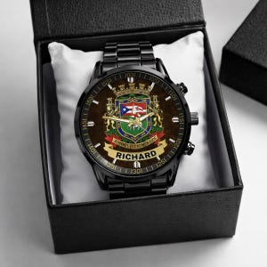 May include: A black wristwatch with a brown face featuring a coat of arms design and the name "RICHARD". The watch is presented in a black box with a white cushion. The watch has a black metal band.