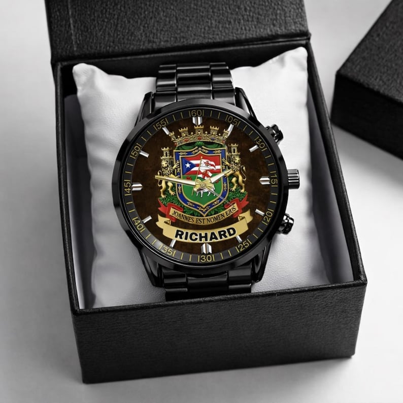 May include: A black wristwatch with a brown face featuring a coat of arms design and the name "RICHARD". The watch is presented in a black box with a white cushion. The watch has a black metal band.