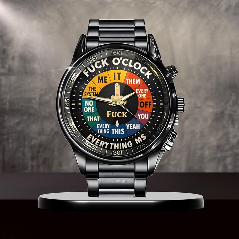 May include: A black wristwatch with a unique dial design. The watch face features the text "FUCK O'CLOCK" with various phrases in a colorful segmented circle. The watch has a black metal band and a silver-colored stand.
