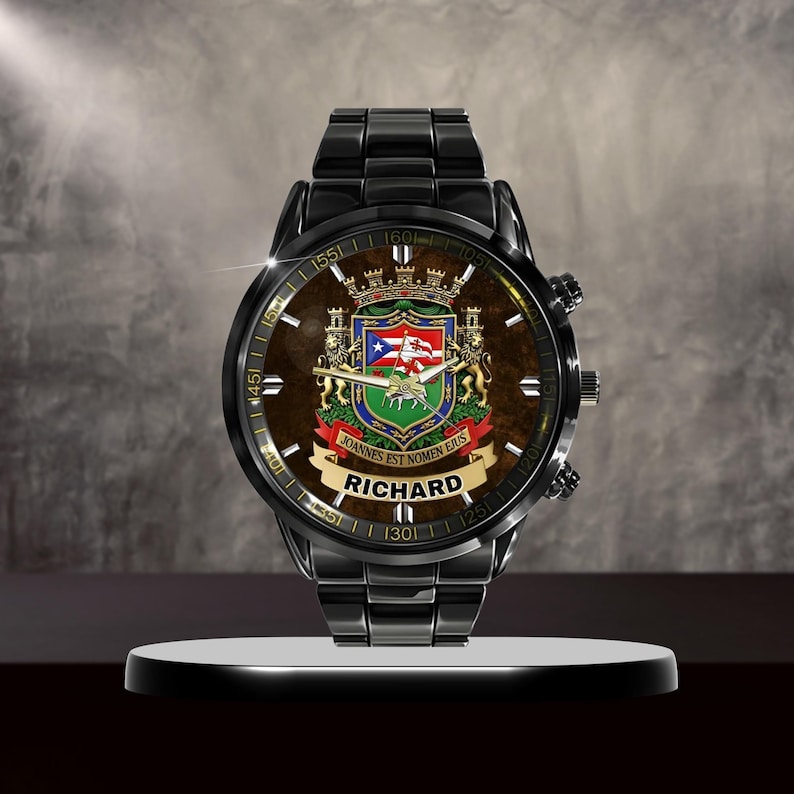 May include: A black wristwatch with a brown face featuring a coat of arms design and the name "RICHARD" on a banner. The watch has a black metal band and is displayed on a white stand.