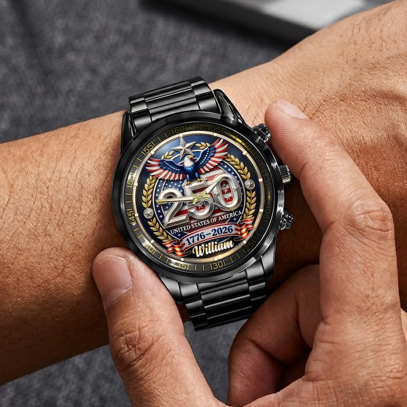 May include: Black wristwatch with a detailed face featuring the text "250 UNITED STATES OF AMERICA 1776-2026 William" and an eagle emblem. The watch has a black metal band and a round black bezel.
