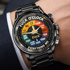 May include: Black wristwatch with a round face featuring the text "FUCK O'CLOCK" and various other phrases. The watch has a black metal band and a black face with colorful segments. The watch hands are gold.