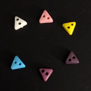 May include: Six triangle-shaped buttons with two holes each. The buttons are in different colors: white, pink, yellow, blue, purple, and a darker purple.