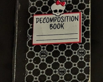 May include: A black notebook with a silver and black checkered pattern. The front cover features a white skull with a red bow and the text "Decomposition Book".