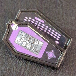 May include: A black and purple coffin-shaped phone with a purple screen that says "Clawdeen" and has icons for apps. The phone is closed and has a black star with a purple circle in the center.