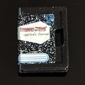 Könnte beinhalten: Ein schwarz-weißes Notizbuch mit dem Titel "Monster High Spectra's Journal" auf dem Cover.