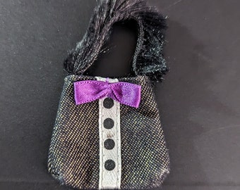 Könnte beinhalten: Eine kleine schwarze und goldene Glitzerhandtasche mit einer violetten Schleife und einem schwarzen, flauschigen Griff.