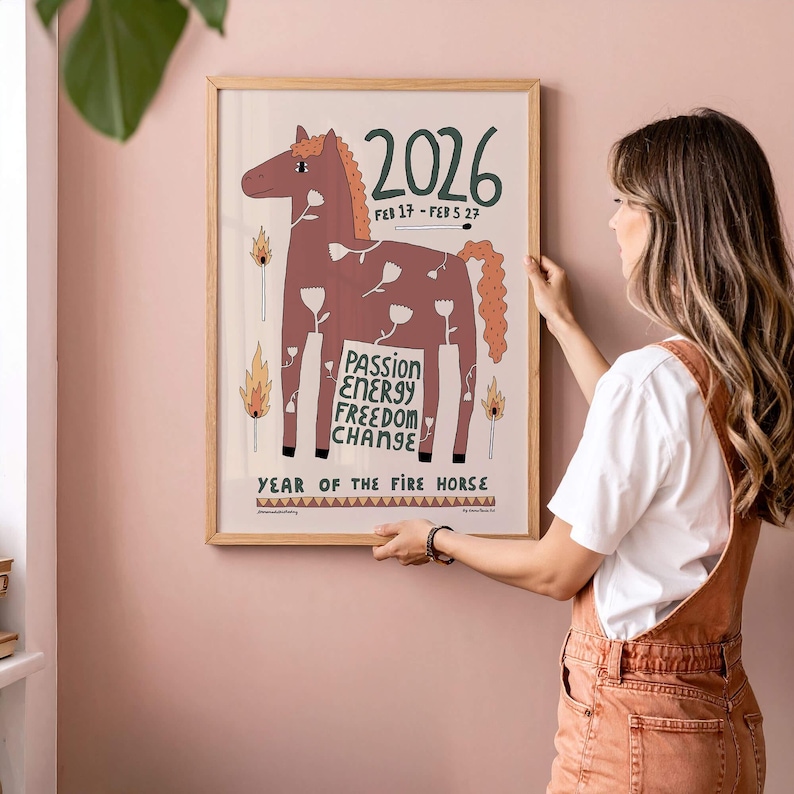May include: A framed wall poster featuring a brown horse illustration with white flower patterns, the text 2026, FEB 17 - FEB 5 27, PASSION ENERGY FREEDOM CHANGE, and YEAR OF THE FIRE HORSE, accompanied by matchstick and flame graphics.