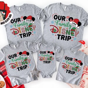 Puede incluir: Una colecci&oacute;n de camisetas grises y un body con el texto "OUR Family DISNEY TRIP" en un dise&ntilde;o colorido. Cada camiseta tiene un nombre en un gorro de Pap&aacute; Noel de Mickey Mouse. Se incluye una bolsa de tela gratuita de 38x38 cm.