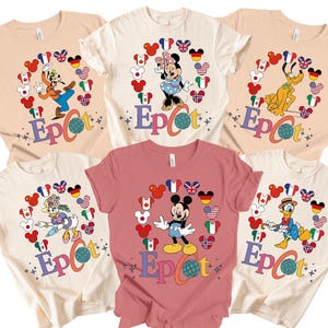May include: A collection of t-shirts featuring Disney characters like Goofy, Minnie Mouse, Pluto, Daisy Duck, Mickey Mouse, and Donald Duck. Each shirt has a character surrounded by flags and the word "Epcot" in colorful letters.