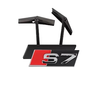 May include: Black and red S7 emblem with mounting hardware. The emblem features a silver "S7" logo on a black background with a red accent. The mounting hardware is black.