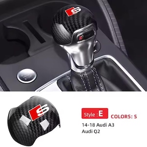 Puede incluir: Pomo de palanca de cambios de fibra de carbono con el logotipo "S" rojo y blanco. El pomo se muestra en el interior de un coche, con una funda de palanca de cambios de cuero y un botón de arranque/parada. También se muestra un pomo suelto.