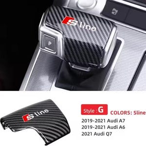 May include: Carbon fiber gear shift cover with the "S line" logo in red and white. Compatible with Audi A7, A6, and Q7 models from 2019-2021. The cover has a textured, patterned design.