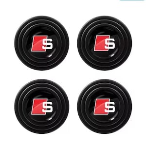 May include: Four black car door protectors with a red and white logo. Each round protector has a ridged outer edge and a glossy finish. The logo features a white "S" inside a red square.