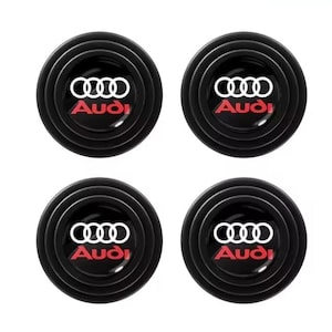 May include: Four black car door protectors with the Audi logo in white and red. Each protector is round with concentric rings and the Audi logo in the center.