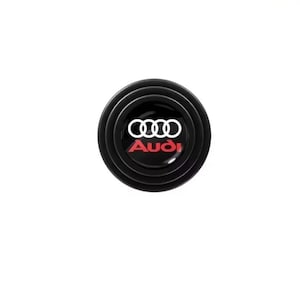 May include: Black, circular car door protector with the Audi logo in white and red. The logo features four interlocking rings above the brand name.
