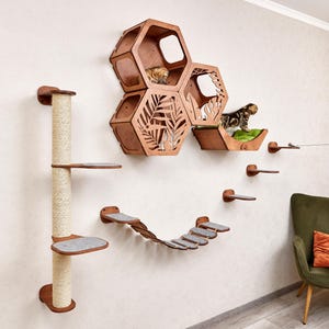 Puede incluir: Un sistema de pared para escalar para gatos de madera con múltiples plataformas, un poste rascador y una casa para gatos en forma de panal. El sistema está montado en una pared de color claro, con dos gatos explorando las estructuras.