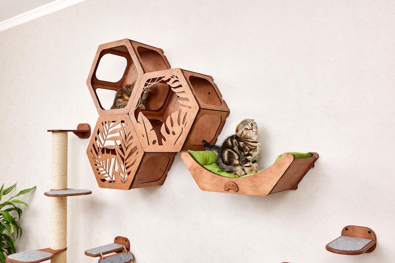 Puede incluir: Juego de muebles para gatos de madera con dise&ntilde;o de panal. El juego incluye una cama para gatos con un coj&iacute;n verde, una estanter&iacute;a de pared y un rascador. Se ven dos gatos.