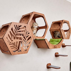 Puede incluir: Juego de muebles para gatos de madera con diseño de panal. El juego incluye múltiples estantes hexagonales, una cama para gatos con un cojín verde y estantes para trepar para gatos. Un gato atigrado está dentro de uno de los estantes.
