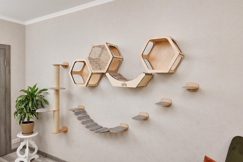 Puede incluir: Un conjunto de muebles para gatos de madera montado en una pared beige. El conjunto incluye estantes hexagonales, un puente curvo, escalones y un rascador. El &aacute;rbol para gatos y los estantes son de madera clara con superficies alfombradas grises.