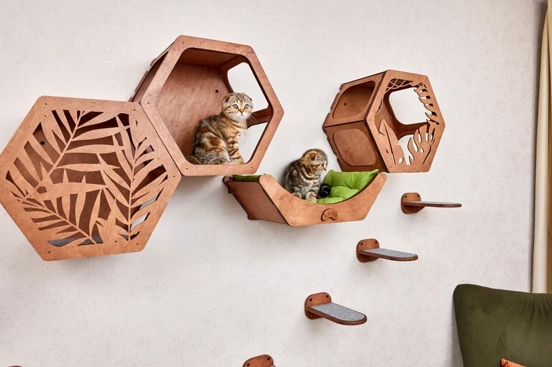 Puede incluir: Juego de muebles para gatos de madera con m&uacute;ltiples casas hexagonales y escalones. Dos gatos est&aacute;n sentados en las casas. Las casas para gatos son marrones con recortes de hojas. Los escalones son marrones con almohadillas grises.