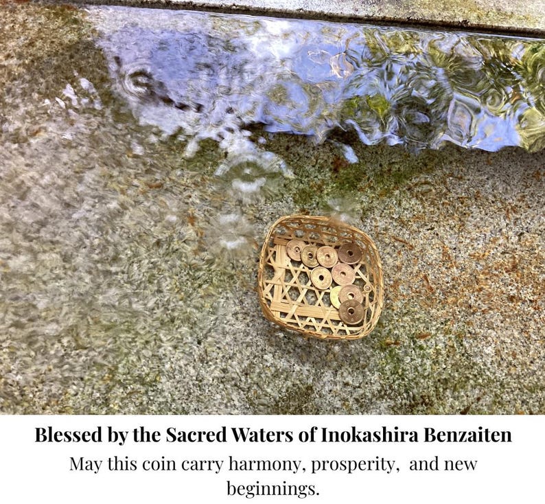 Op de afbeelding: Een geweven mandje gevuld met Japanse munten ligt op een getextureerd stenen oppervlak bij stromend water. De afbeelding bevat de tekst "Blessed by the Sacred Waters of Inokashira Benzaiten" en een boodschap over harmonie en voorspoed.