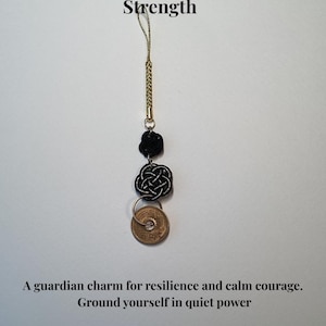 Op de afbeelding: Een zwarte Mizuhiki-bedel met een gouden koord, met twee decoratieve knopen en een Japanse munt. De tekst luidt "Black Mizuhiki - For Protection & Strength" en "A guardian charm for resilience and calm courage."