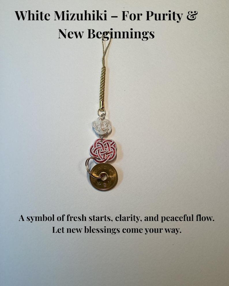 Op de afbeelding: Een Mizuhiki-bedel met witte en rode knopen, een gouden munt en de tekst "White Mizuhiki - For Purity & New Beginnings". De bedel is een symbool van nieuwe starts, helderheid en vrede.