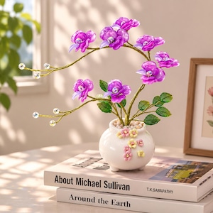 May include: A decorative arrangement featuring vibrant purple flowers with central iridescent crystals, set on thin gold-toned wire stems with small clear beads. The flowers are planted in a small white ceramic pot adorned with tiny pastel floral accents.