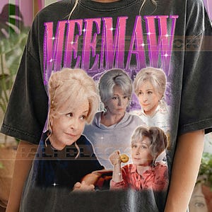 Peut inclure: T-shirt gris foncé avec un graphisme de quatre femmes et le mot "MEEMAW" dans une police rétro rose et violette. Le texte "PEPPER COMFORT COLORS" est imprimé en bas du t-shirt.