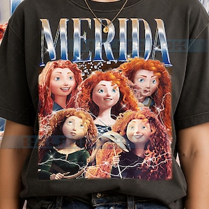 Può includere: T-shirt grigio scuro con una grafica del personaggio Merida del film d'animazione Ribelle - The Brave. La parola "MERIDA" è stampata in alto in un font stilizzato, con immagini di Merida sotto.