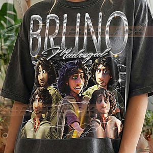 Puede incluir: Camiseta gris oscuro con el nombre "BRUNO Madrigal" en letras plateadas sobre un gráfico del personaje de la película. El gráfico incluye múltiples imágenes del personaje con acentos de rayos. El texto "PEPPER COMFORT COLORS" está en la parte inferior.