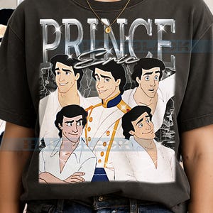 Op de afbeelding: Donkergrijs t-shirt met een afbeelding van Prins Eric uit De Kleine Zeemeermin. Het ontwerp bevat het woord "PRINCE" in zilveren blokletters boven de naam "Eric" in script, samen met meerdere afbeeldingen van het personage.