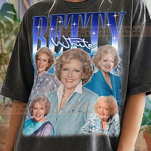 May include: Dark grey t-shirt featuring multiple images of Betty White, with the name "Betty White" in blue and white text. The shirt has a vintage look, with the words "Pepper Comfort Colors" printed at the bottom.